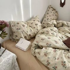 an unmade bed with flowers on it next to a book and some vases