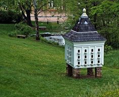 a white bird house sitting on top of a lush green field next to a pond