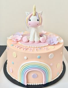 a pink cake with a unicorn on top and rainbow decorations around the edges, sitting on a table