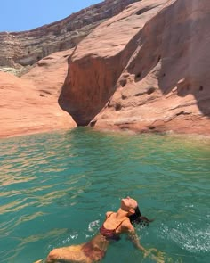 a woman is swimming in the water near some rocks and sand cliffs, with her head above the water's surface