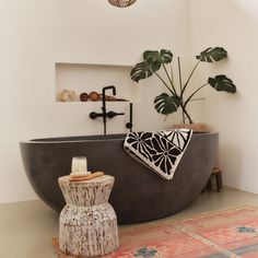 a bathroom with a plant in the bathtub next to a stool and rug on the floor