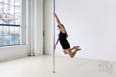 a young woman is practicing pole dancing in an empty room