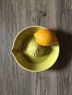 an orange sitting on top of a green bowl next to a slice of lemon in it