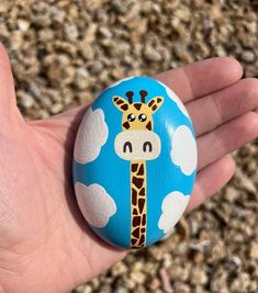 a hand holding a painted rock with a giraffe on it's face