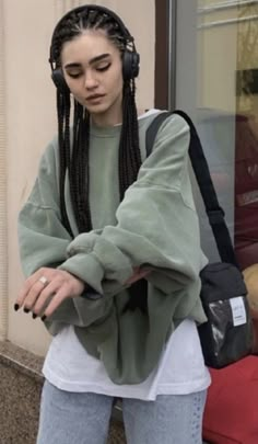 a woman with dreadlocks standing in front of a building wearing headphones and looking at her cell phone