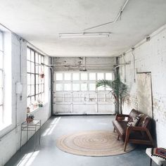 an empty room with a chair, rug and potted plant in the corner on the floor