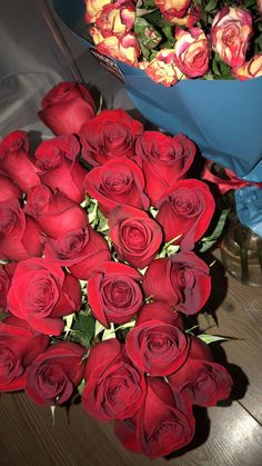 a bouquet of red roses sitting on top of a table next to a vase filled with flowers