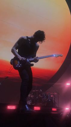 a man standing on top of a stage with a guitar in front of an orange and red background