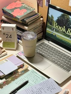 a laptop computer sitting on top of a desk next to a pile of books and papers