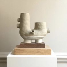 a white sculpture sitting on top of a wooden block in front of a beige wall