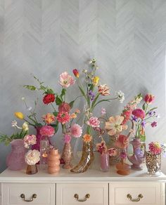 a white dresser topped with lots of vases filled with flowers