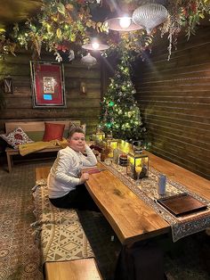 a woman sitting at a table in a room with christmas decorations on the walls and lights hanging from the ceiling