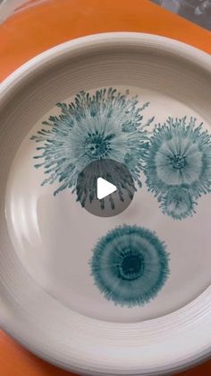 a white bowl with blue flowers painted on the side and an orange table cloth behind it