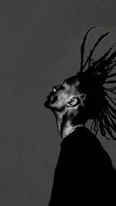 a black and white photo of a man with dreadlocks looking up at the sky