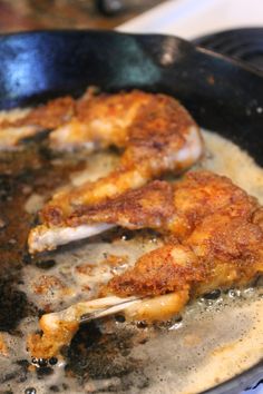 two pieces of chicken cooking in a skillet on the stove with some oil over it