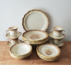 a table topped with lots of white and gold dinnerware on top of a wooden table