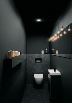 a bathroom with black walls and flooring is lit by lights above the toilet bowl