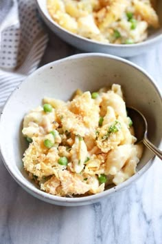 two bowls filled with pasta and peas on top of a marble countertop next to a silver spoon