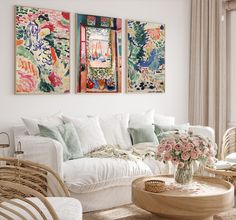 a living room with wicker furniture and paintings on the wall above it's windows