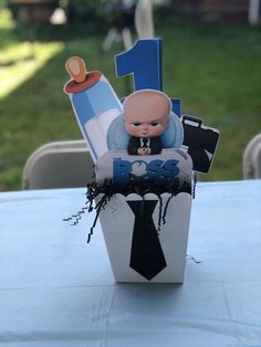 a baby's first birthday cake in a box on a blue table cloth covered table