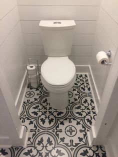 a white toilet sitting inside of a bathroom next to a roll of toilet paper on the floor