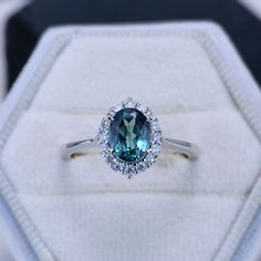 a ring with a blue stone surrounded by white diamonds in a velvet box on top of a table