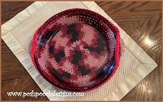 a red glass bowl sitting on top of a white napkin covered placemat in front of a wooden table