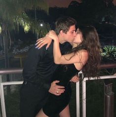 a man kissing a woman on the cheek while standing next to a railing at night