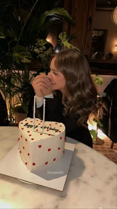 a woman sitting in front of a white cake with red hearts on it and candles sticking out