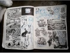 an open comic book with drawings on the pages and in front of a cat's paw