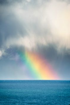 a rainbow appears over the ocean on a cloudy day