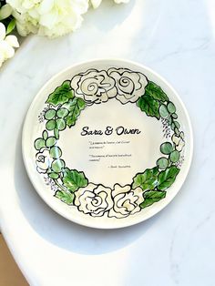 a plate with flowers on it sitting on a table next to some white flowers and greenery