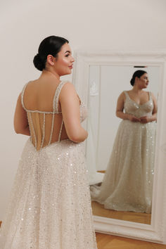 a woman in a wedding dress looking at herself in the mirror with her back to the camera