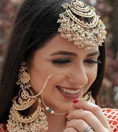 a woman in a red and gold outfit with jewelry on her head, smiling at the camera