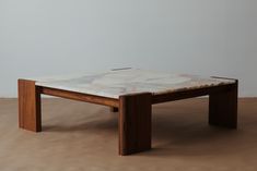 a marble top coffee table with wooden legs on a brown carpeted floor in front of a white wall