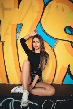 a beautiful young woman sitting on the ground in front of graffiti