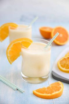 two glasses filled with orange juice next to sliced oranges on a blue tablecloth