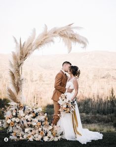 a bride and groom kissing in front of an arch decorated with feathers