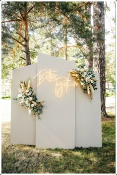 an illuminated sign with flowers and greenery on it in the middle of a forest