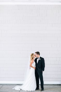 a bride and groom kissing in front of a white brick wall