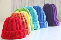 crocheted beanies lined up on a white table with the colors of the rainbow