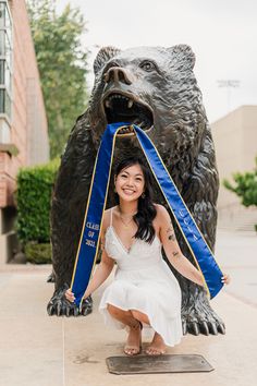 a woman poses in front of a statue of a bear with a blue ribbon around it's neck