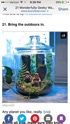 a glass jar filled with plants and two small figurines sitting on top of a table