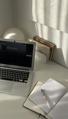 an open laptop computer sitting on top of a desk next to a notepad and pen