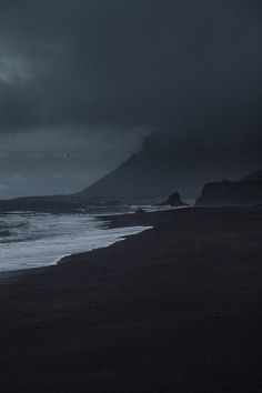 a person walking on the beach at night with an umbrella over their head and dark clouds in the background