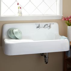 a white sink sitting under a window next to a vase with pink flowers in it