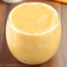 a smoothie in a glass sitting on a table next to some carrots and an orange