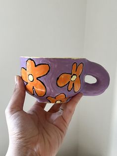 a hand holding a purple cup with orange flowers painted on the outside and inside it