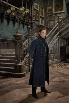 a man in a blue coat standing next to a stair case with paintings on the wall