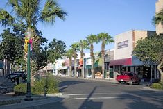 a red truck driving down a street next to tall buildings and palm trees in front of it